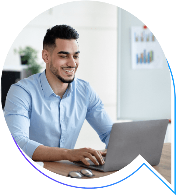 Smiling man in blue shirt working on a laptop in a modern office setting.