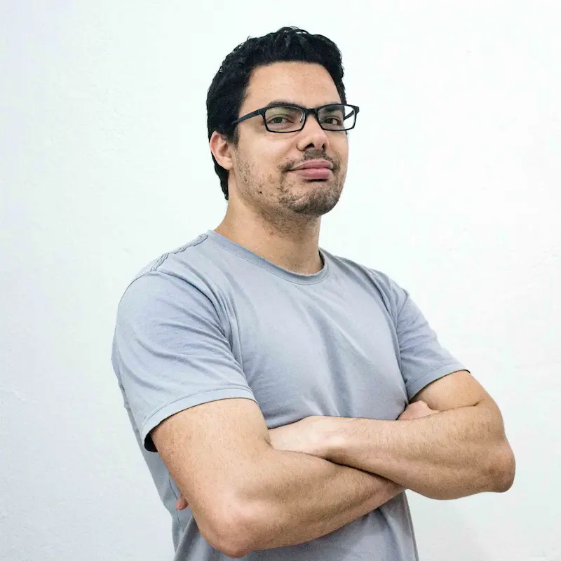 Man with glasses wearing a grey t-shirt stands confidently with arms crossed.