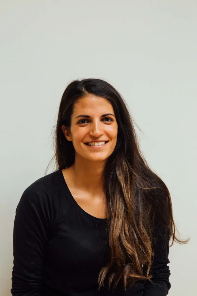 Woman with long brown hair smiling in a portrait against a neutral background.