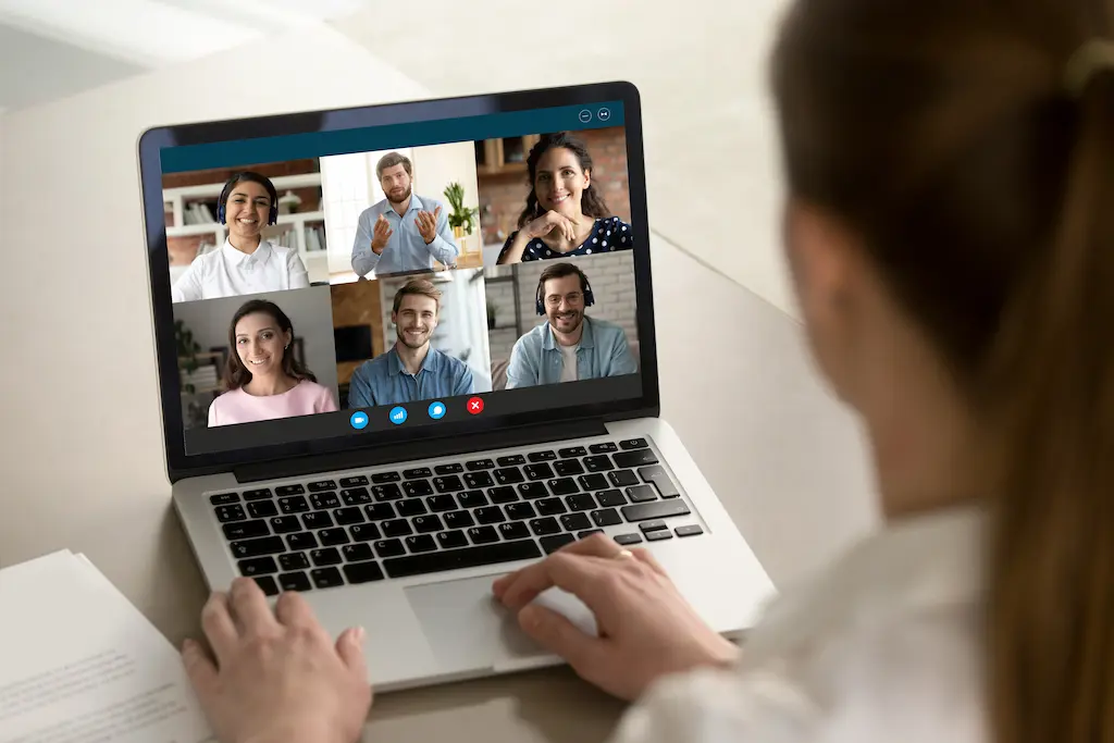 Person participating in a virtual meeting on a laptop with six colleagues visible on the screen.