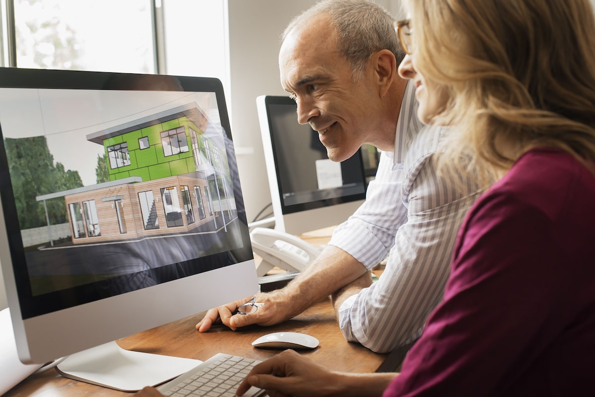 Two colleagues collaborate on architectural design at a computer, focused on a 3D house model.