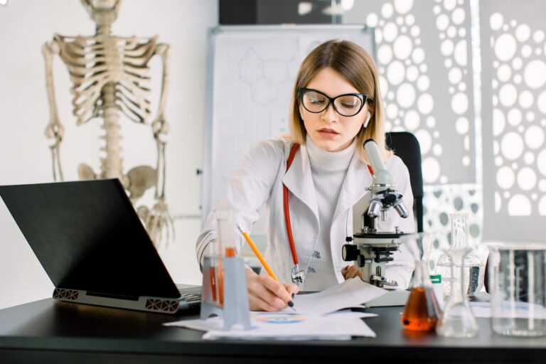 Medical professional using laptop and microscope in modern lab.