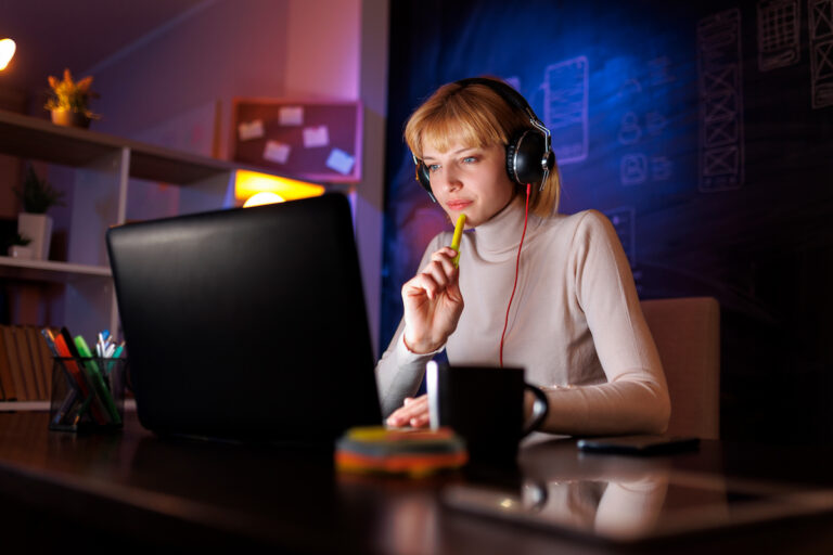 Woman with headphones working on a laptop at night in a creative workspace.