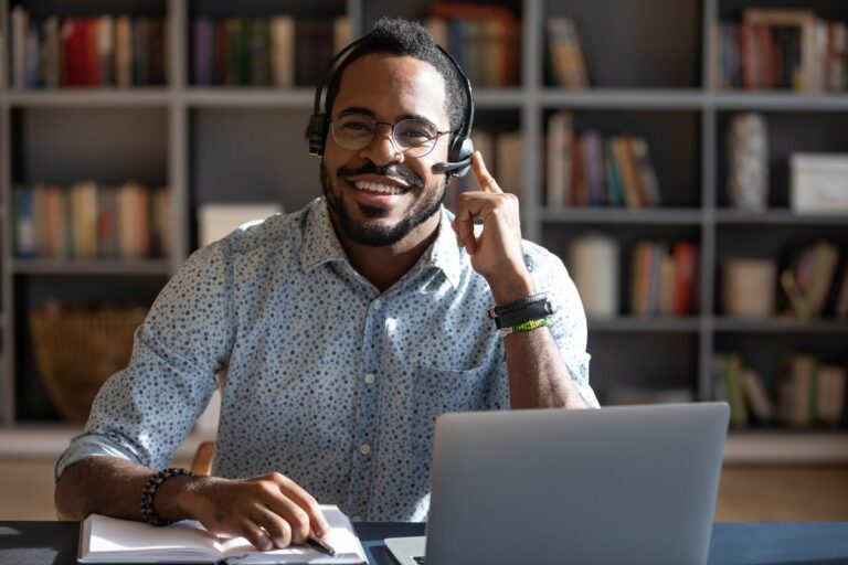 Smiling virtual assistant using a headset and laptop in a modern office setting.