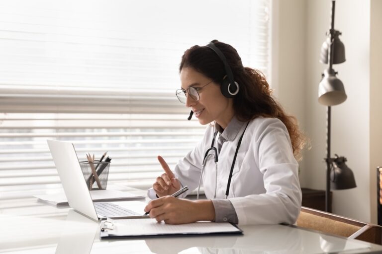 Healthcare professional using a laptop with a headset for virtual assistance.
