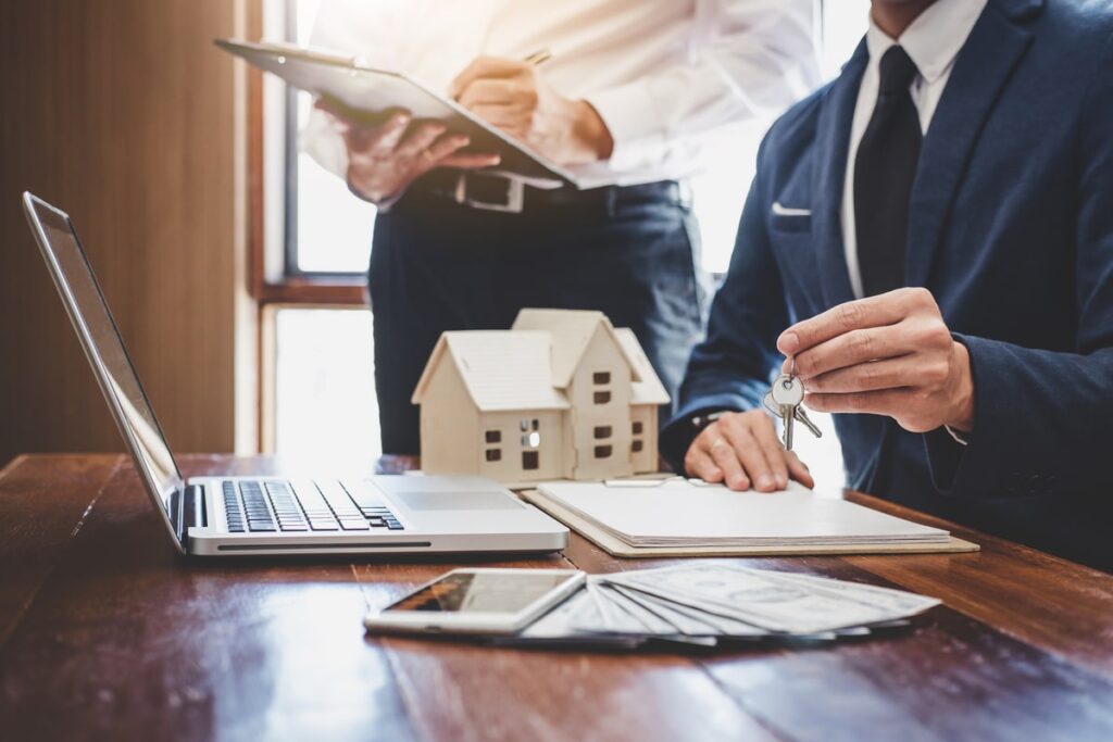 virtual assistant real estate working on laptop next to small model of a house.