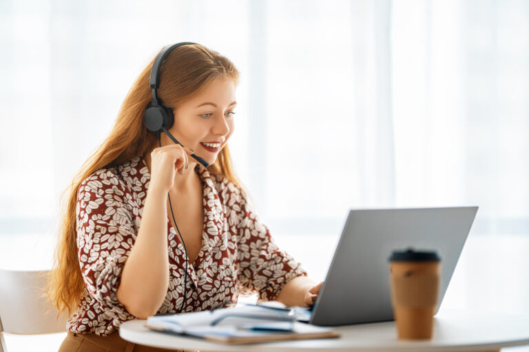 A smiling woman wearing a headset while working on a laptop, representing virtual assistant services.