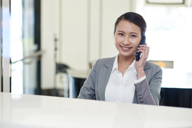 Smiling administrative assistant talking on the phone in a professional office setting.