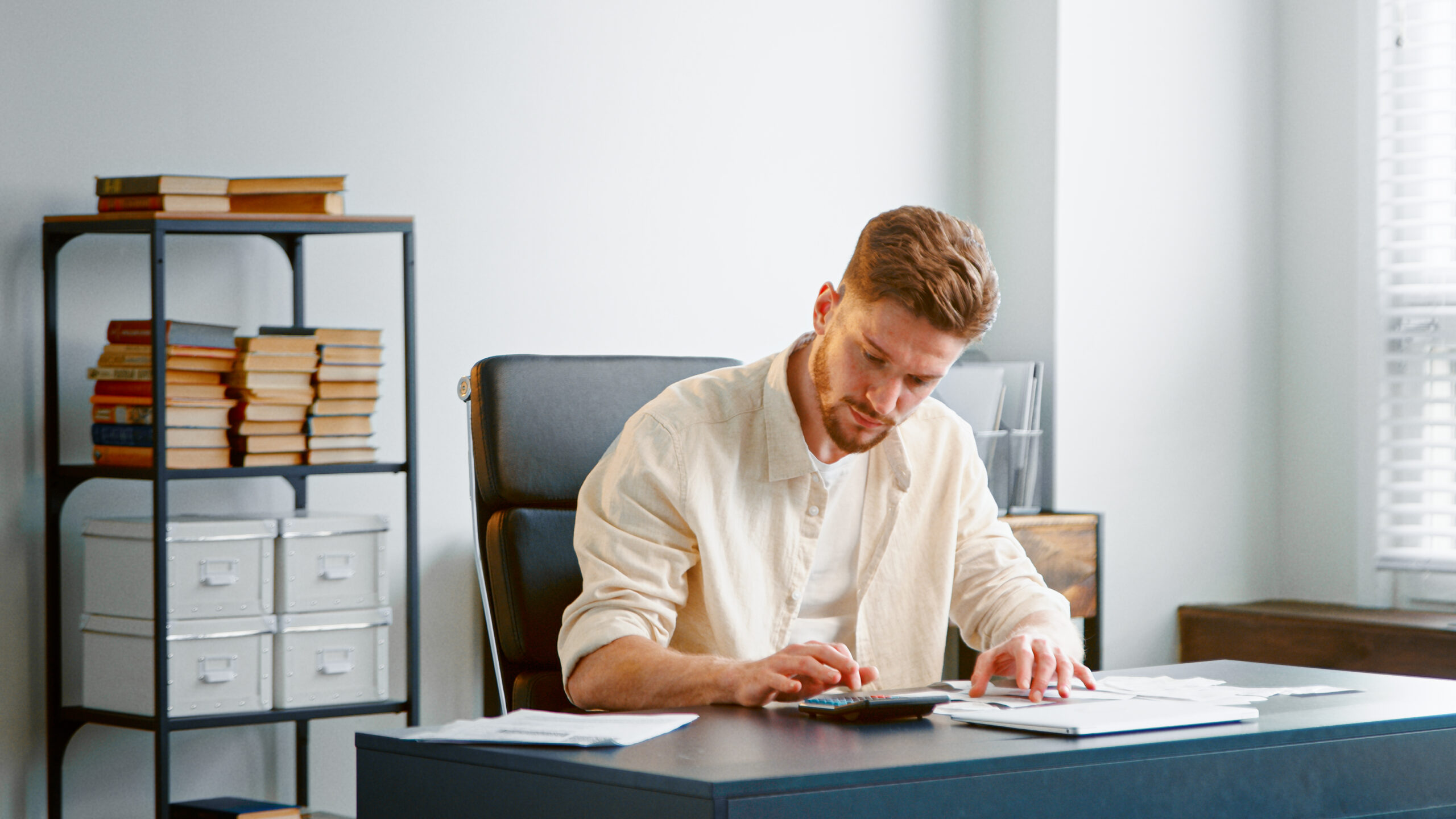 Focused administrative assistant working on financial calculations at a desk in a modern office.