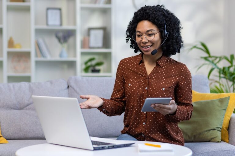African American female teacher with curly hair using a laptop and headset for online in a cozy home setting.
