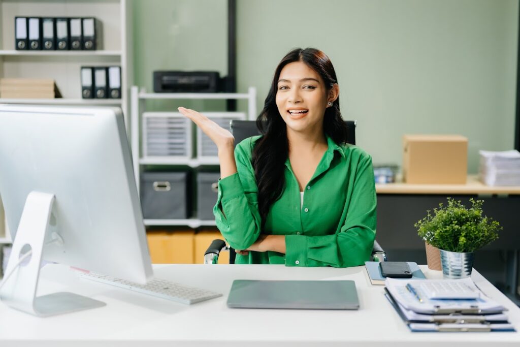 Smiling virtual office assistant at a desk, gesturing while working remotely.