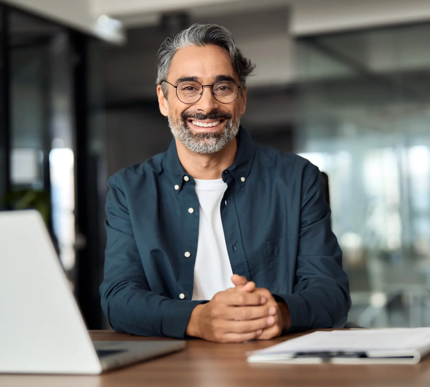 Professional man smiling at desk with laptop and documents.