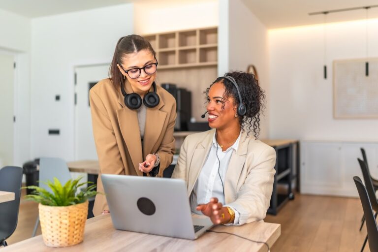 Two businesswomen in an office setting engaging over a laptop for a collaborative project.