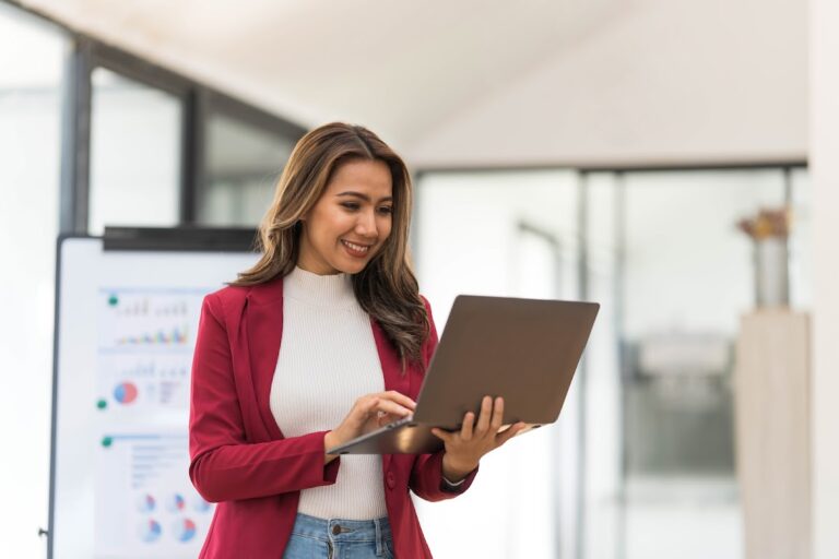 Woman in red blazer holding a laptop in modern home office.