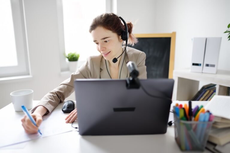 Woman with headset working on laptop and writing