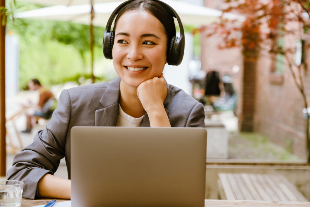 Woman smiling with headphones and laptop outdoors
